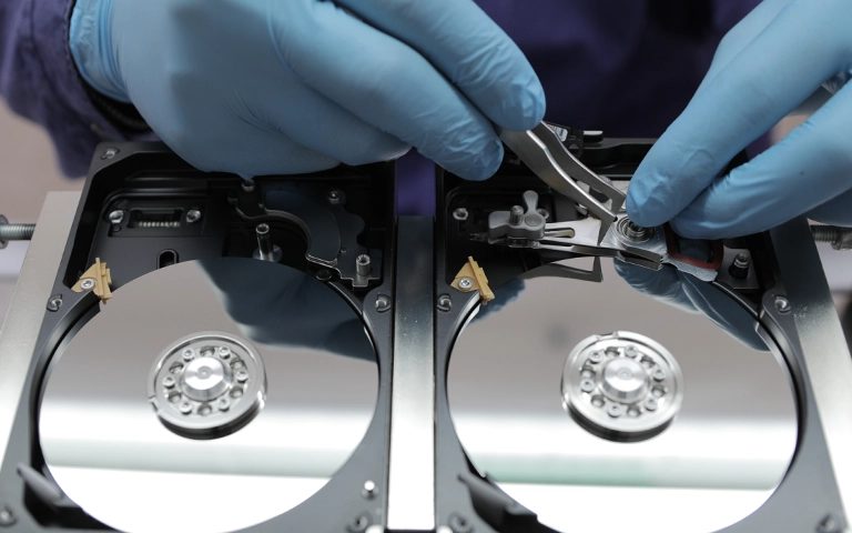 Mavi eldivenli teknisyen iki açık hard disk arasında okuma-yazma kafası grubunu aktarıyor