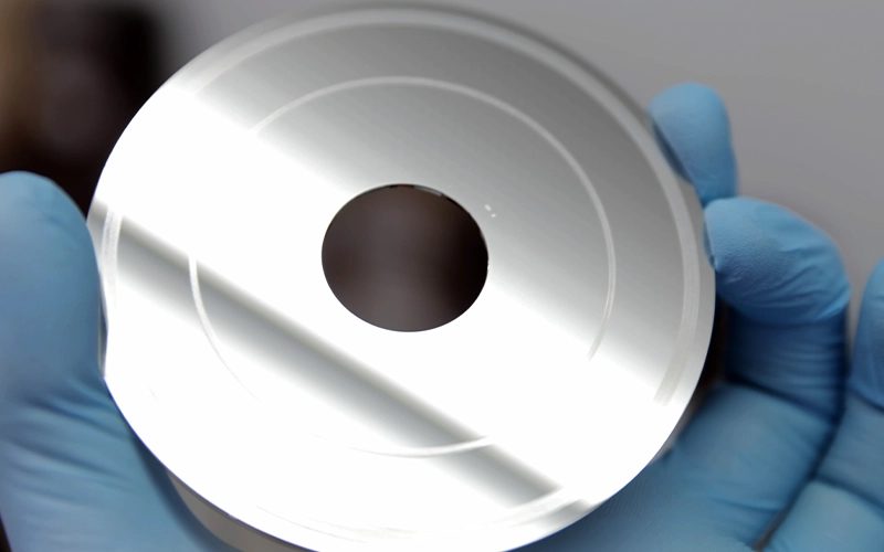 Mavi eldivenli elde tutulan, yüzeyinde dairesel çizikler görülen hard disk plakası